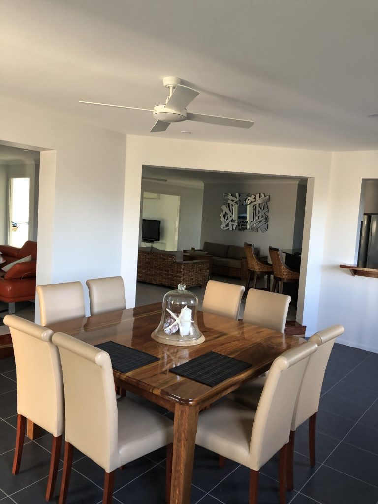 Dining room with a timber table and cream chairs, opening to a living area