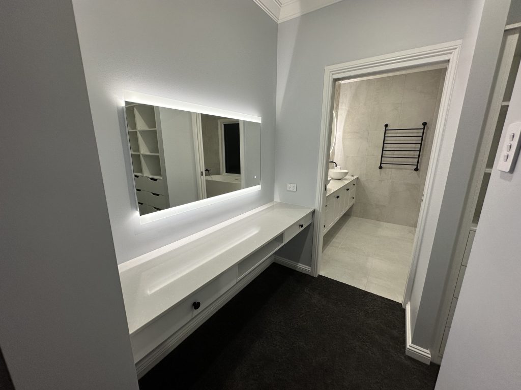 White built-in vanity bench with a backlit mirror beside an ensuite doorway