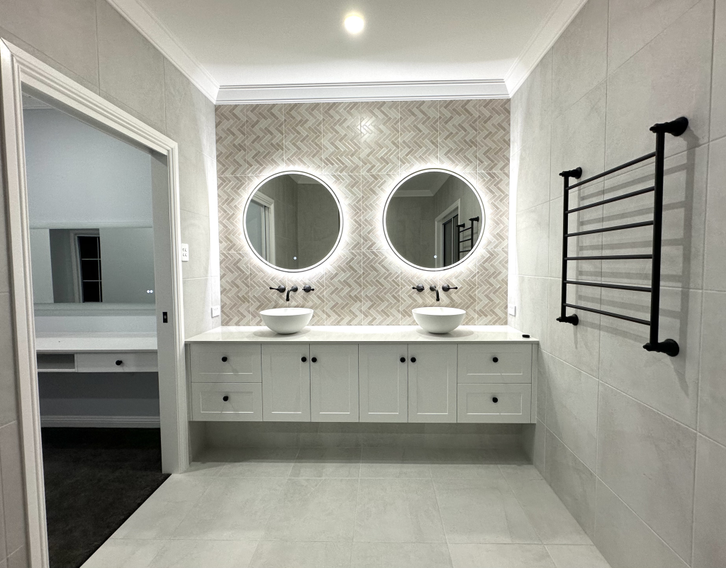 Bathroom seen through a doorway, with a double vanity and round backlit mirrors